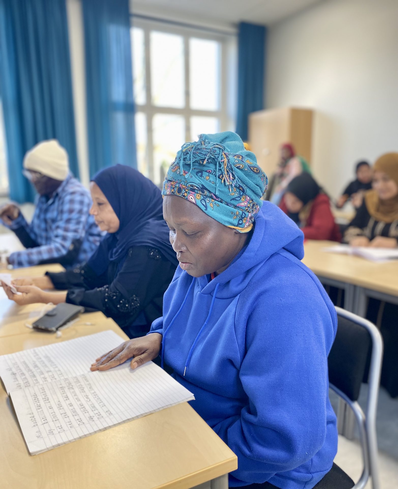En sfi- elev sitter och läser i ett klassrum med andra sfi-elever.